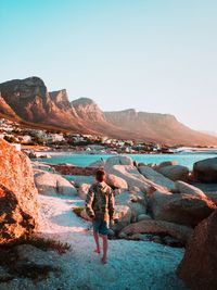 Rear view of woman standing on rock against sky
