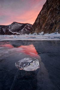 Frozen lake against mountain during sunset