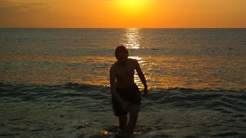 Rear view of man standing on beach during sunset