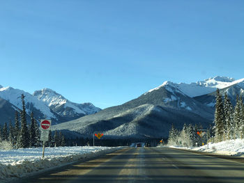 Road by snowcapped mountains against clear sky