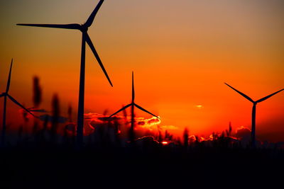 Silhouette of wind turbines on field against orange sky