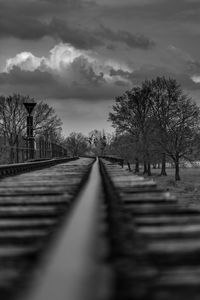 Surface level of railroad track amidst bare trees against sky