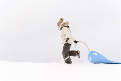 Girl pulling sled while walking on snow covered land against sky