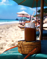 Close-up of drink on deck chair at beach against sky