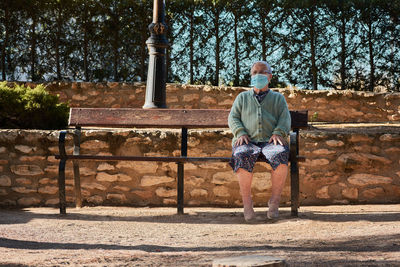 Older woman sitting on a park bench with her mask on