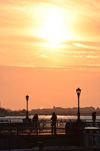 Silhouette people on promenade against river during sunset