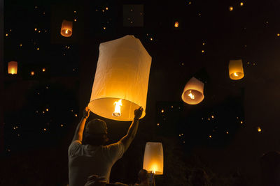 Low angle view of man releasing paper lantern at night