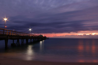 Illuminated pier over sea against sky during sunset