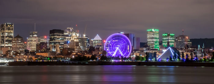 Illuminated city by river against sky at night