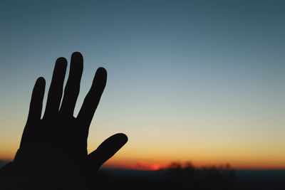 Silhouette hand against sky during sunset