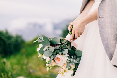 Midsection of bride holding flower bouquet on field