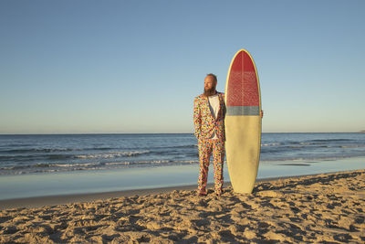 Fashionable man with surfboard looking away while standing against sea