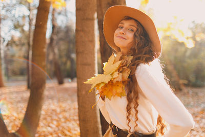 Portrait of young woman standing by tree trunk