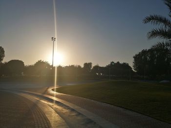 Street by trees against sky during sunset