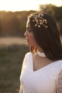 Side view of elegant young female in boho bridal maxi dress and wreath in green woods and looking away