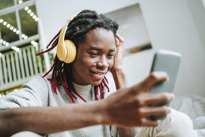 Smiling young man wearing headphones using smart phone at home