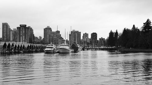 Boats in water by buildings in vancouver  against sky