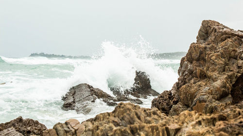 Waves splashing on rocks against clear sky