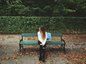 Full length of young woman wearing torn jeans sitting on bench at augarten