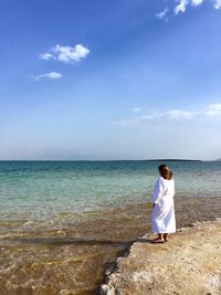 Rear view of woman standing at beach against sky