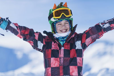 Portrait of happy boy with arms outstretched standing against snowcapped mountains