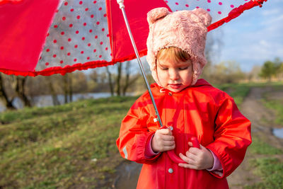 Child plays with umbrella after the rain in red rubber boots and a raincoat.