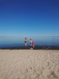 People on beach against clear blue sky