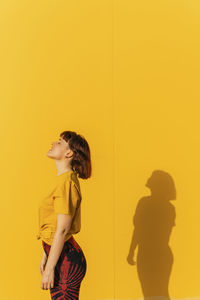 Woman standing with eyes closed by yellow wall