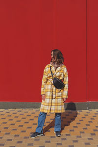Beautiful caucasian girl in a yellow coat on a bright red background in sunbeams. autumn city outfit