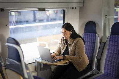 Mid adult woman in train using laptop