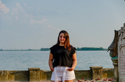 Portrait of young woman standing in sea against sky