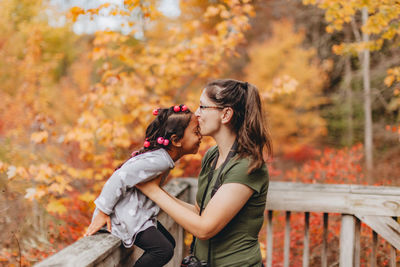 Mother embracing with daughter while standing against autumn trees