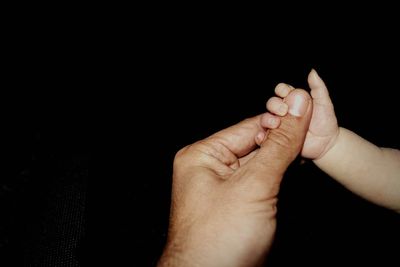 Cropped baby hand holding thumb of father against black background