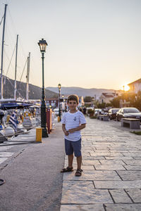 Full length portrait of boy standing on street against sky