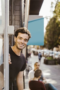 Portrait of smiling male deli owner peeking from doorway