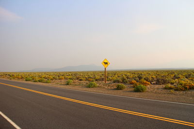 Empty road by field against sky on sunny day