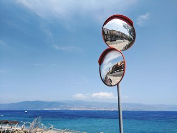 Low angle view of road mirrors at beach against blue sky