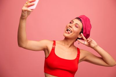 Portrait of young woman taking selfie against pink background