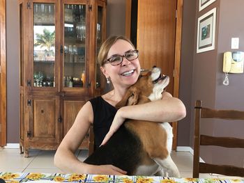 Portrait of smiling woman embracing dog at home