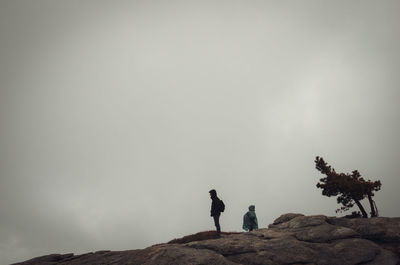 Low angle view of men standing on rock against sky