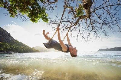 Happy man on swing enjoying holiday. beautiful sunset on beach in seychelles.