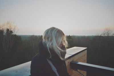 Blond woman standing by retaining wall against sky during sunset