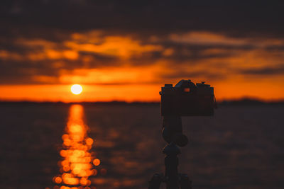 Close-up of silhouette camera against sky during sunset