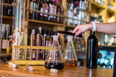 Midsection of woman holding glass bottles on table