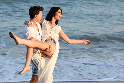 Boyfriend carrying girlfriend while standing at beach