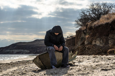 Full length of man sitting on rock against sky