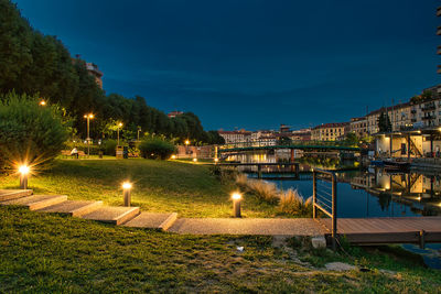 Illuminated buildings by river against sky at night