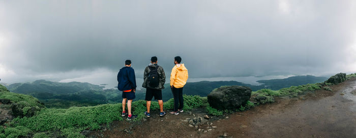 Rear view of men standing on mountain against sky