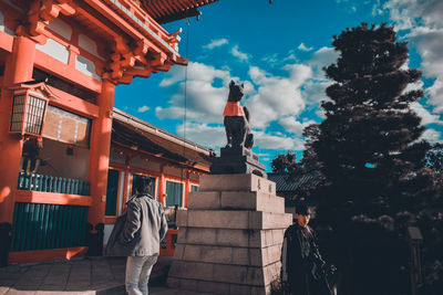 Low angle view of man standing by sculpture against sky