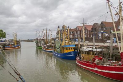 Sailboats moored on harbor against sky in city